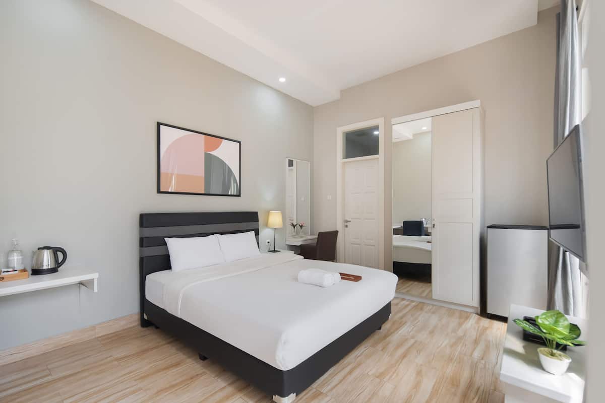 A modern hotel room with a large bed, a bedside table with a lamp, a small shelf with toiletries, a mirror, and a TV.