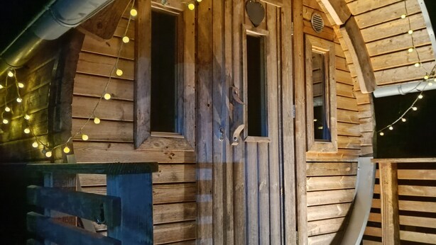 Una cabaña de madera con techo curvo, una puerta con ventanal en forma de corazón y luces colgantes.