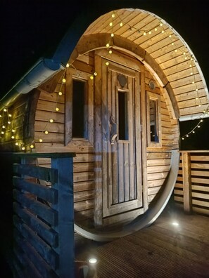 A wooden cabin with a curved roof, a door, and string lights. - Cozy vacation apartment with barrel sauna and hot tub (Laubach)