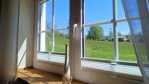 Una habitación con un ventanal grande, un jarrón en el alféizar y vistas a un paisaje verde.