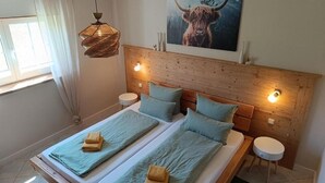 Una cama doble con dos almohadas, una mesita de noche, una lámpara de pared y un cuadro de un yak.