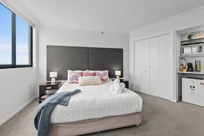A modern bedroom with a large bed, a dark headboard, bedside lamps, and a wardrobe with shelves. - Central Studio | Walk to River, Shops & Dining (Brisbane)