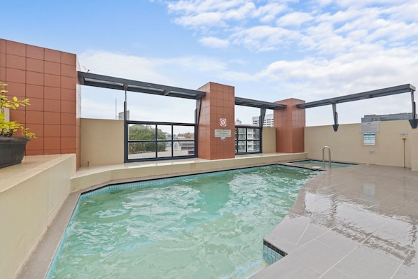 An indoor swimming pool with a clear view of the surrounding buildings, a sign indicating a pool depth of 1.25 meters, and a spa area. - Central Studio | Walk to River, Shops & Dining (Brisbane)
