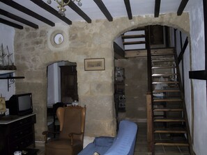 A room with a stone wall, a wooden chair, a blue sofa, a television, and a staircase. - Casa Bohemio - Tabarca (Tabarca)