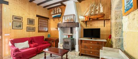 A wooden-furnished living room with a red sofa, a wooden coffee table, a television, and a ship model.