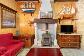 A cozy room with a red sofa, a wooden chest, a fireplace, and a television. - Casa Bohemio - Tabarca (Tabarca)