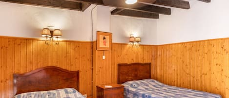 A room with two wooden beds, a wooden nightstand, a ceiling fan, and wall-mounted lamps.