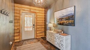 Un interior de madera con una puerta, una consola blanca decorada con objetos y un cuadro de paisaje en la pared.