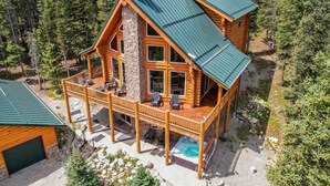 Una cabaña de troncos con terraza, jacuzzi y chimenea de piedra.