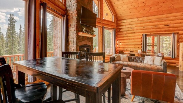 Interior de una cabaña de troncos con una mesa de comedor, sofá y chimenea.