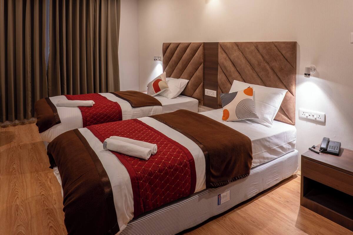 Ein Hotelzimmer mit zwei Betten, Holzboden, einem großen Fenster mit Vorhängen und einer Wandleuchte.
