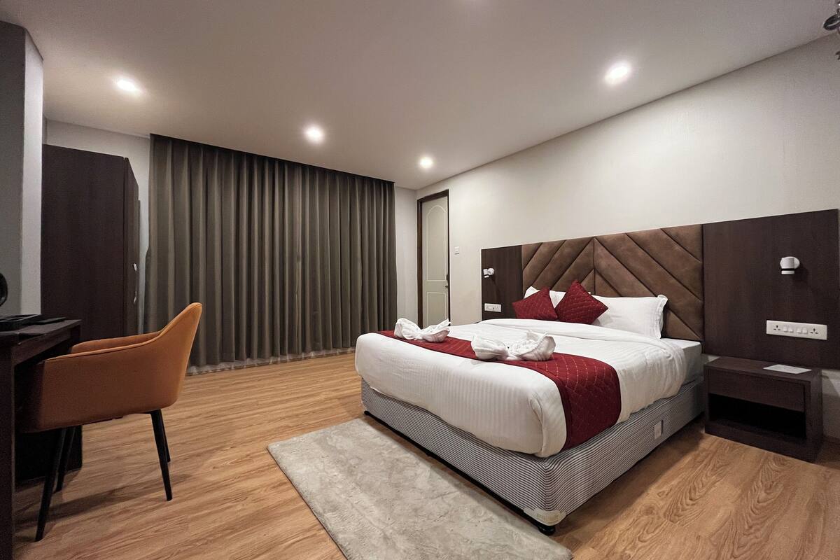 Ein modernes Hotelzimmer mit Bett, Schreibtisch, Stuhl und großem Fenster mit Vorhängen.
