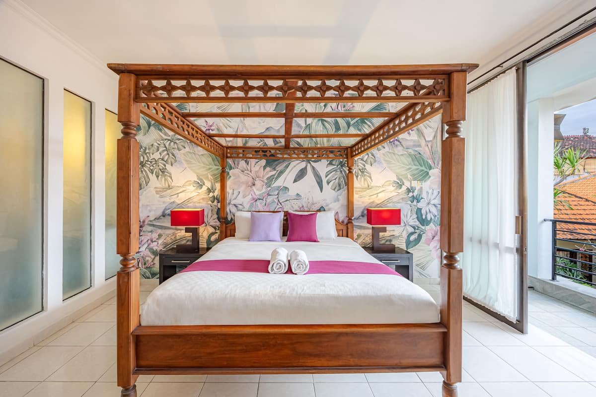A four-poster bed with a floral mural, two nightstands with lamps, and a view of the outside.