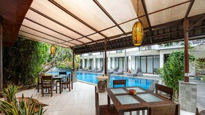 A covered outdoor area with a pool, wooden furniture, and potted plants. - Cove Puri Maharani (Denpasar)