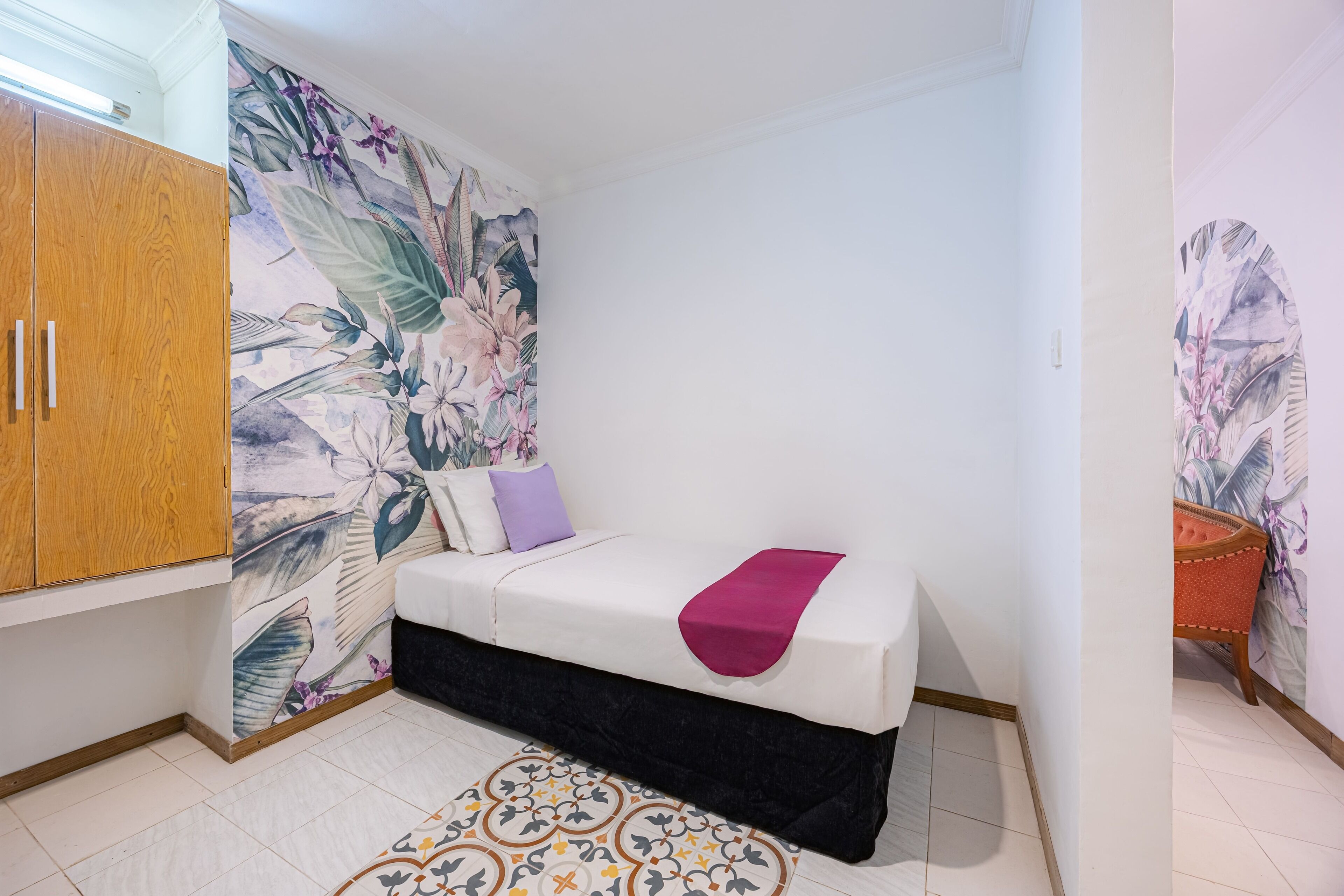 A bedroom with a bed, a wardrobe, a floral wall mural, and a patterned rug.
