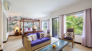 A room with a glass coffee table, a sofa, a chair, and a canopy bed. - Cove Puri Maharani (Denpasar)