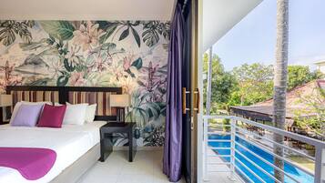Une chambre d’hôtel avec un lit, une table de chevet, une lampe, une fresque murale aux motifs tropicaux et un balcon donnant sur une piscine.