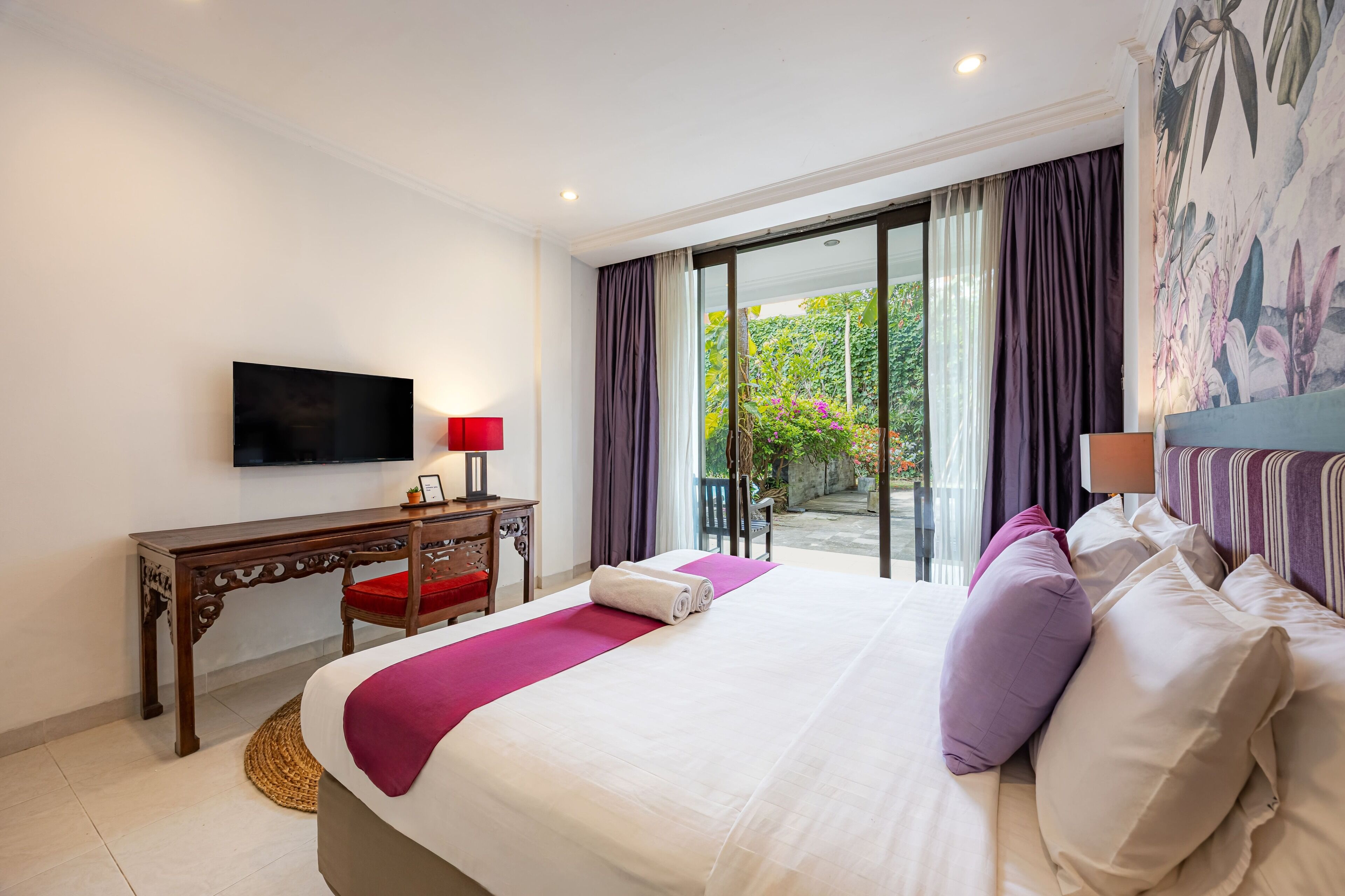 A hotel room with a bed, a desk, a television, and a view of the outdoors.