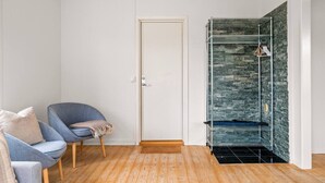 A room with a wooden floor, a white door, a blue chair with a cushion, and a metal rack against a textured wall.