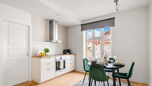A modern kitchen with white cabinets, a stainless steel range hood, and a dining area with green chairs and a round table.