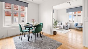 A modern living room with a dining area, featuring a grey rug, green chairs, and a potted plant.