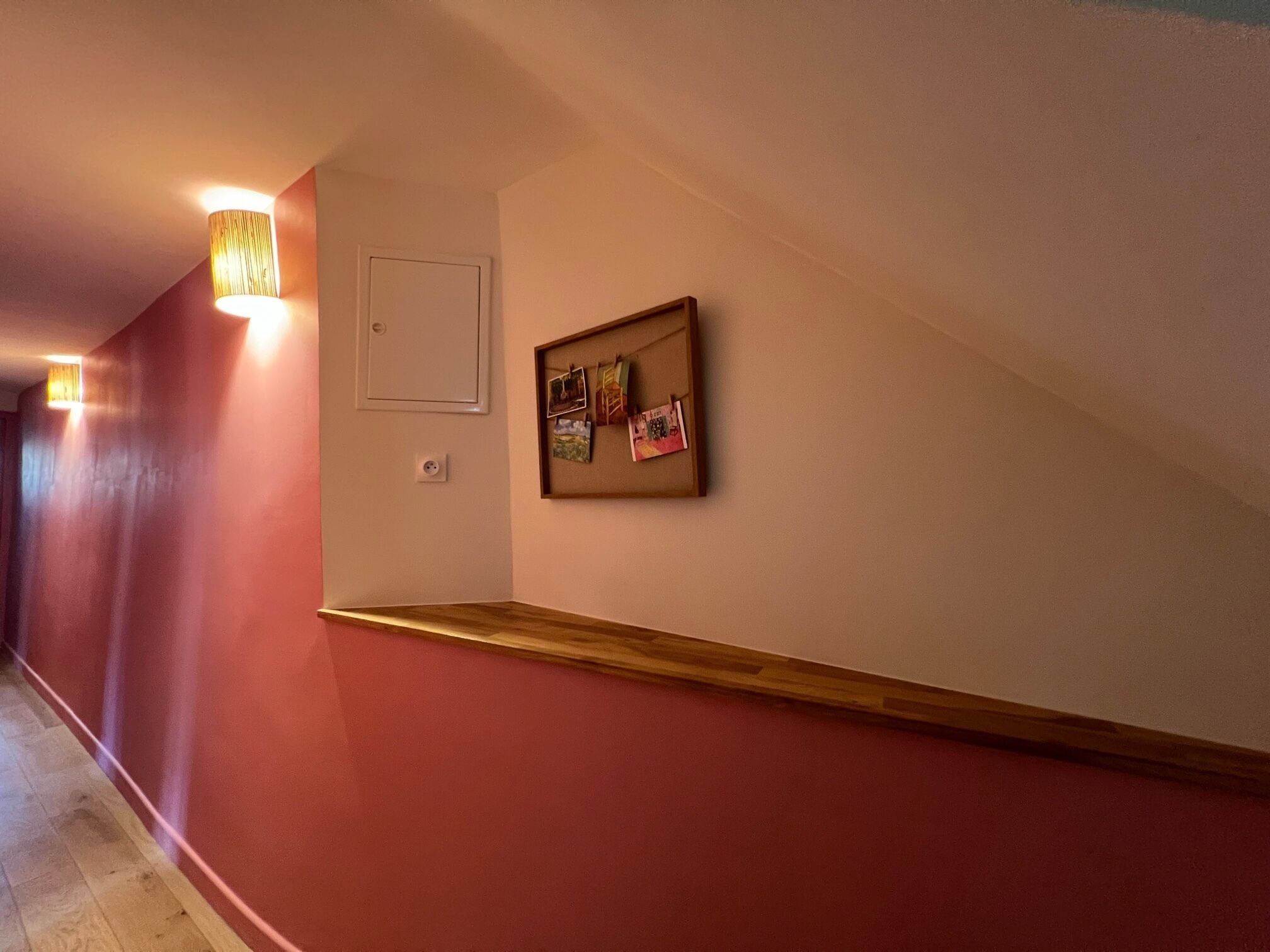 A hallway with a wooden bench, a wall-mounted light fixture, and a bulletin board with pictures.