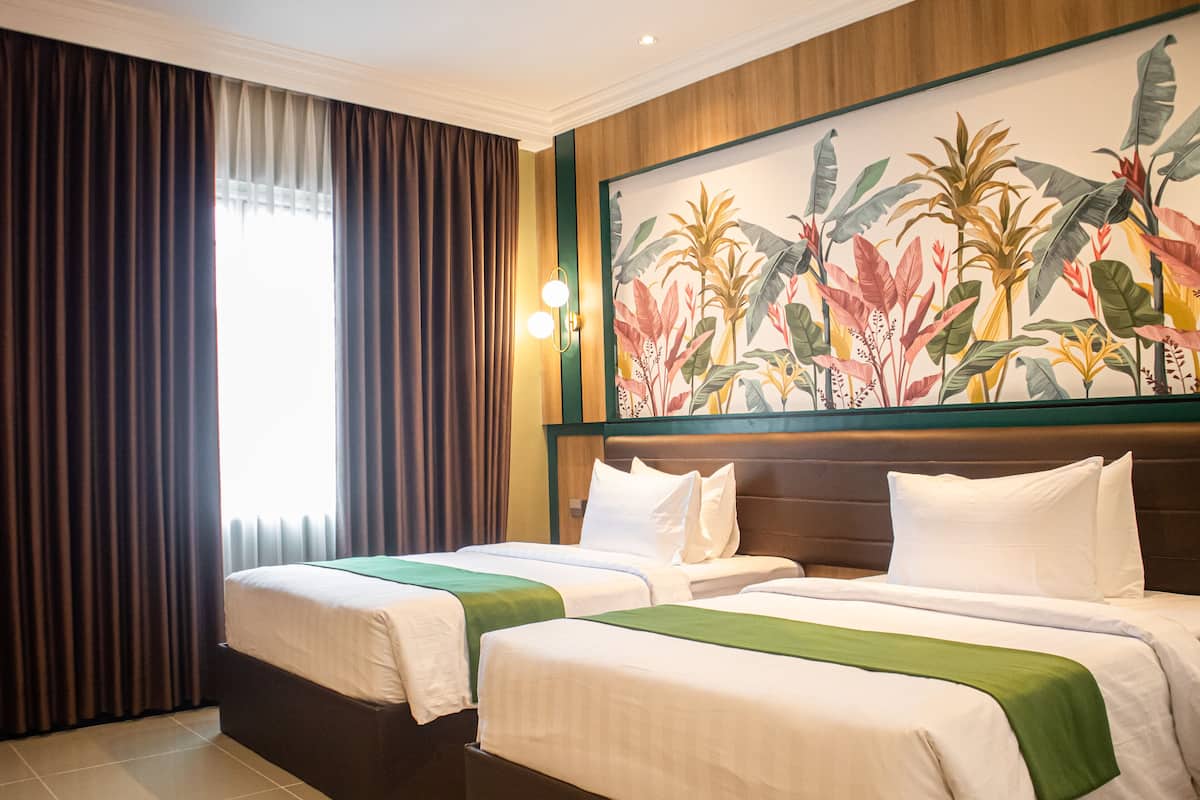 Quarto de hotel com duas camas, um grande mural tropical e vista para o exterior através de cortinas leves.