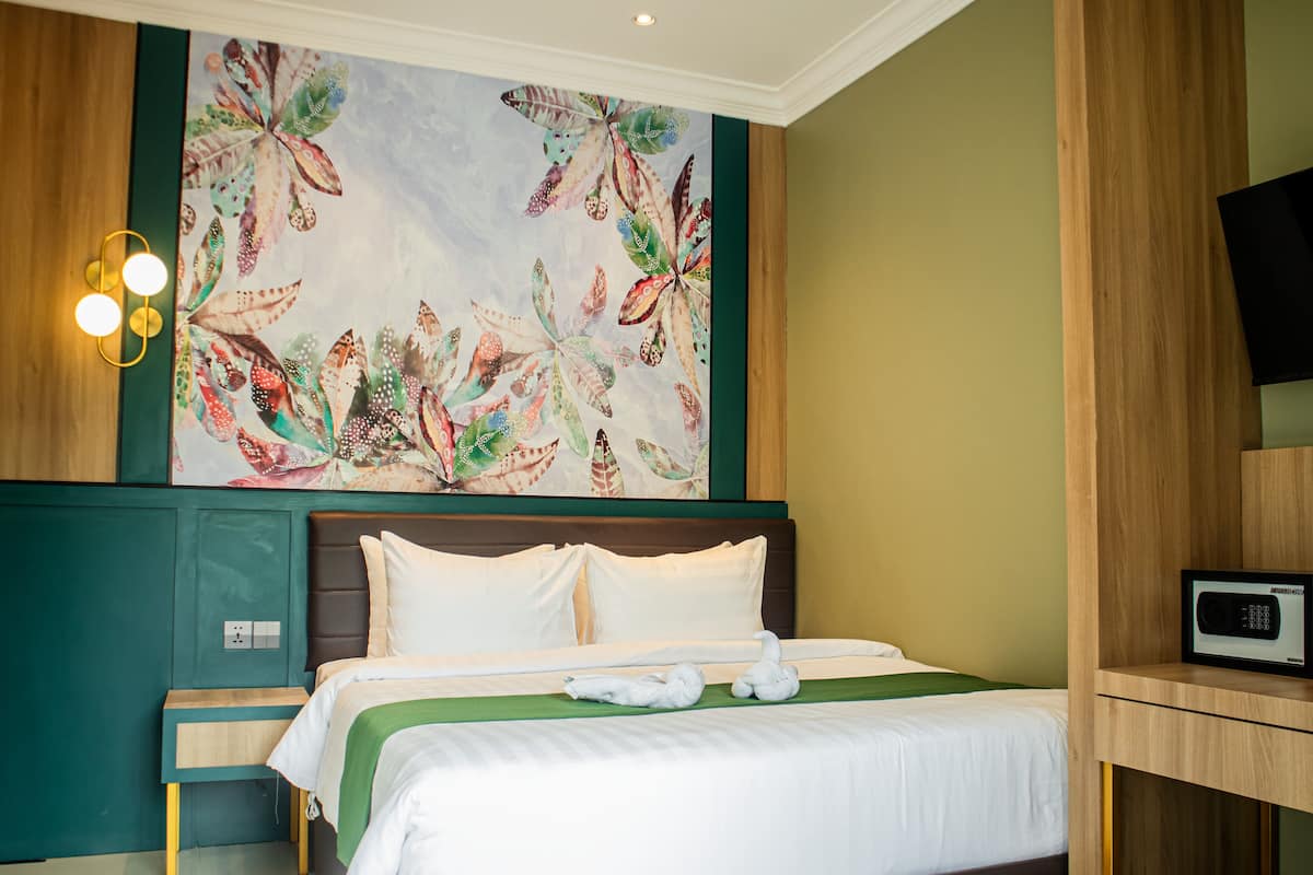 Quarto de hotel com uma cama, parede verde, pintura de borboletas e uma mesa de cabeceira.