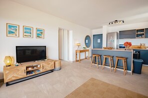 Een moderne woonkamer met een televisie, een houten tv-meubel en een keukenhoek met krukken en een spoelbak.