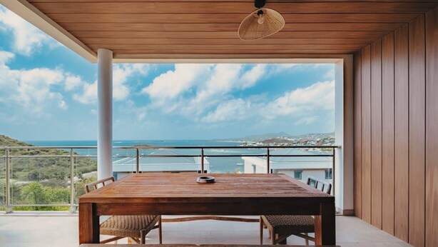A wooden table with chairs on a balcony overlooking a coastal view. - New! Magnificent sea-view apartment in Grand Cayes - 5 min from  Pinel island (saint-martin)