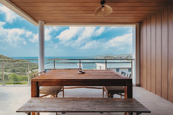A wooden table with chairs on a balcony overlooking a coastal view.