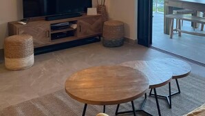 A modern living room with a flat-screen TV, a round wooden table, and a ceiling light fixture. - New! Magnificent sea-view apartment in Grand Cayes - 5 min from  Pinel island (saint-martin)