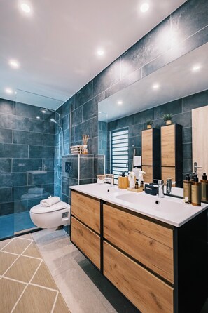 A modern bathroom with dark tiles, a white sink, wooden cabinets, and a large mirror.