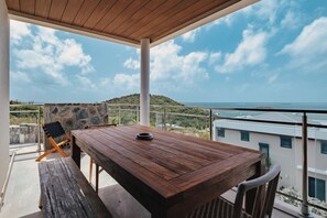 Un tavolo e una panca in legno su un balcone con vista sul mare e sulle colline.