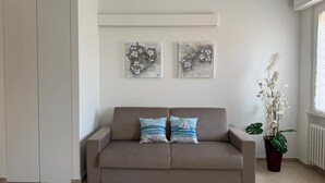 Un salon aux couleurs neutres, avec un canapé beige, deux œuvres d’art accrochées au mur et une plante en pot.
