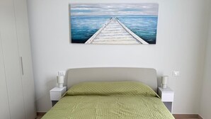 Une chambre à coucher comprenant un lit, une table de chevet, une commode, une armoire et un tableau représentant une jetée s’avançant dans la mer.