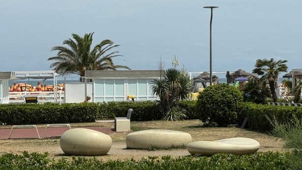 Une zone située en bord de mer, dotée d’un espace extérieur moderne avec des sièges, des palmiers et un bâtiment aux grandes fenêtres.