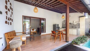 Un espacio exterior moderno con un banco de madera, una mesa de comedor y sillas. Hay una piscina a la derecha.