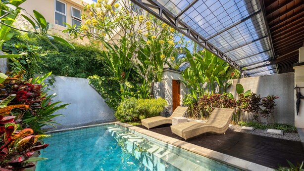 Una piscina con sillones de descanso y abundante vegetación.