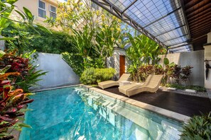 A swimming pool with lounge chairs and lush greenery. -  Cove Belle Asana (Tibubeneng)