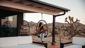 Un área de estar al aire libre moderna con sofás blancos, una chimenea y sillas colgantes.