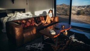 Una habitación con una cama grande, un sofá de cuero, una mesa de centro y vistas a un paisaje desértico.