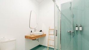 Een moderne badkamer met toilet, wastafel, spiegel, douche en een douchecabine met glazen wanden.