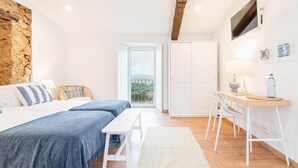 Een slaapkamer met een bed, een bureau, een stoel, een stenen muur en een uitzicht door een deur.