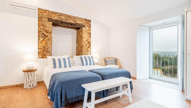Een slaapkamer met twee bedden, een stenen muur, een witte bank en uitzicht op het omliggende landschap.