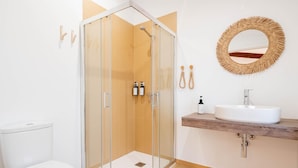 A bathroom with a glass-enclosed shower, a toilet, a sink with a wooden countertop, and a round mirror on the wall. - Room '2' with Shared Pool (Fortios)