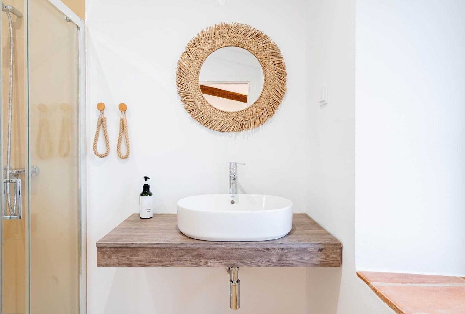 A bathroom with a round mirror, a white sink, and a wooden countertop.