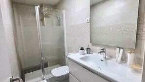 A modern bathroom with a glass-enclosed shower, a white sink with a mirror above it, and a toilet. - Oshun Valdecanillas (Madrid)