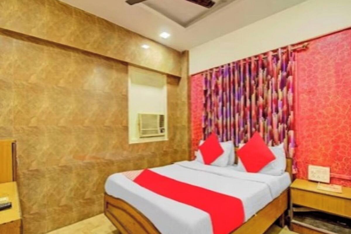 Un dormitorio con cama de madera, ropa de cama roja y blanca, una cortina roja y una mesita de noche pequeña con una lámpara.