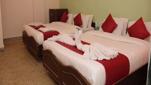 Ein Hotelzimmer mit drei Betten, jeweils mit roter und weißer Bettwäsche und Handtüchern.